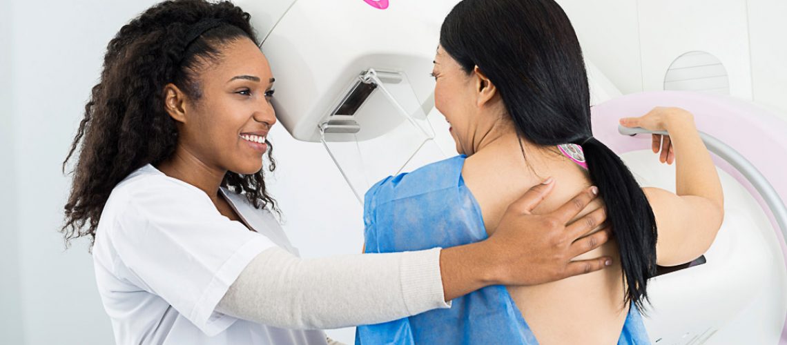Happy female doctor assisting mature woman undergoing mammogram X-ray test in hospital